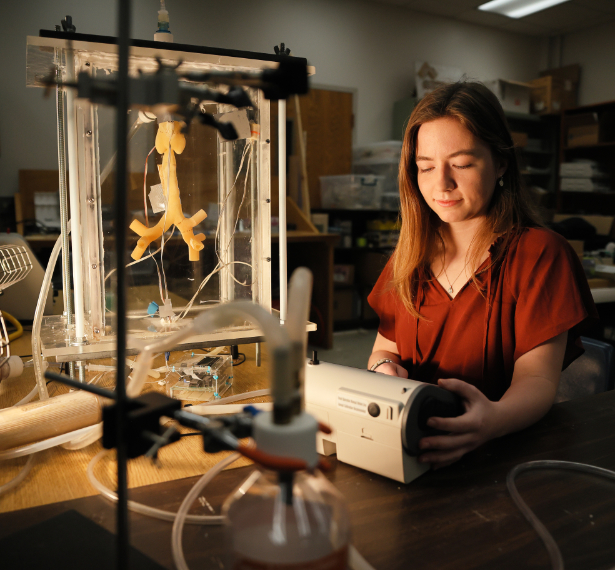 A young woman in a red shirt sits in a dark room, with nebulizer equipment around her.