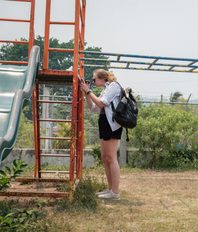 A Mercer student with a backpack inspects an orange-painted ladder to the monkey bars at an outdoor playground.