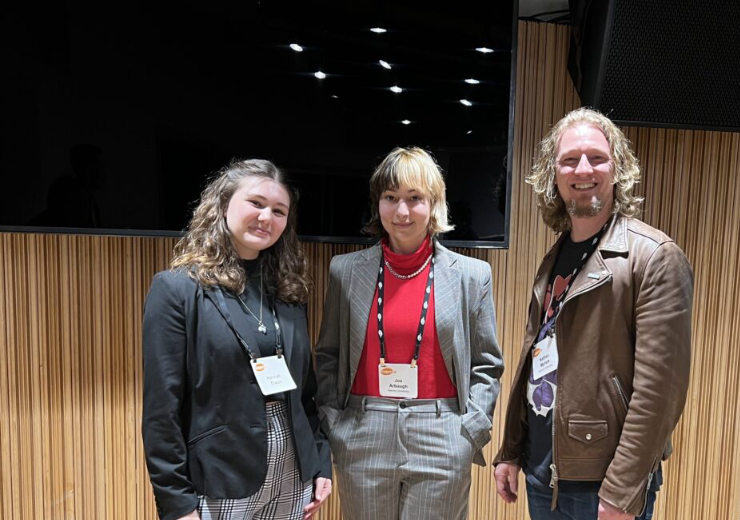 Two Mercer students and their professor indoors at a conference.