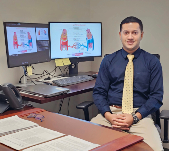 Raquibul Hasan sits in front of two computer monitors displaying blood vessels.